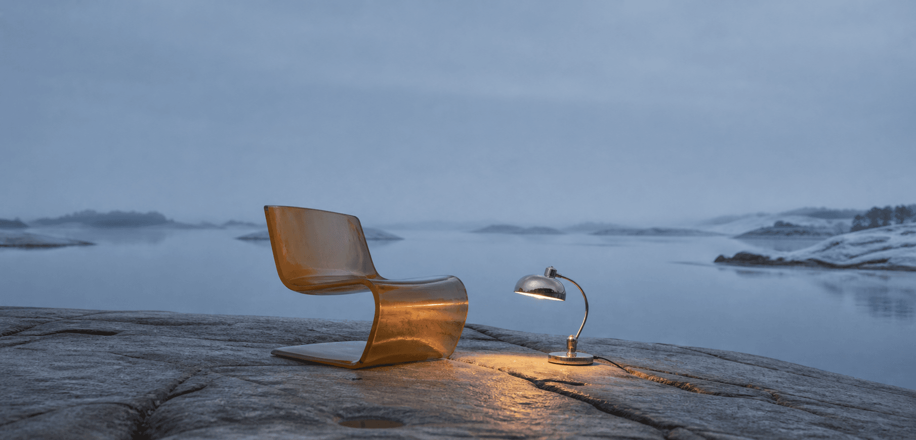 An amber chair and chrome lamp shown in a coastal landscape